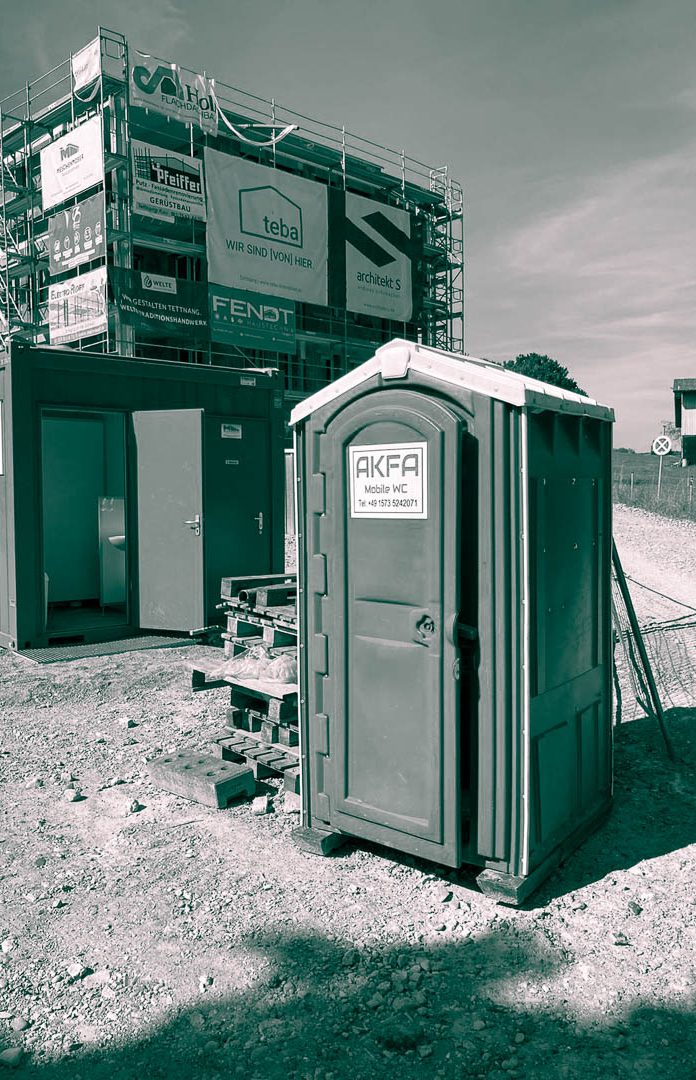 Baustellen WC, Pipi Box, Baustellen Klo Baugelände mit einem mobilen Toilettenhäuschen und Containern im Hintergrund.